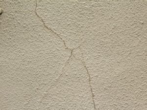 ベージュ色のリシン仕上げ外壁に斜め方向に広がる複数のひび割れ